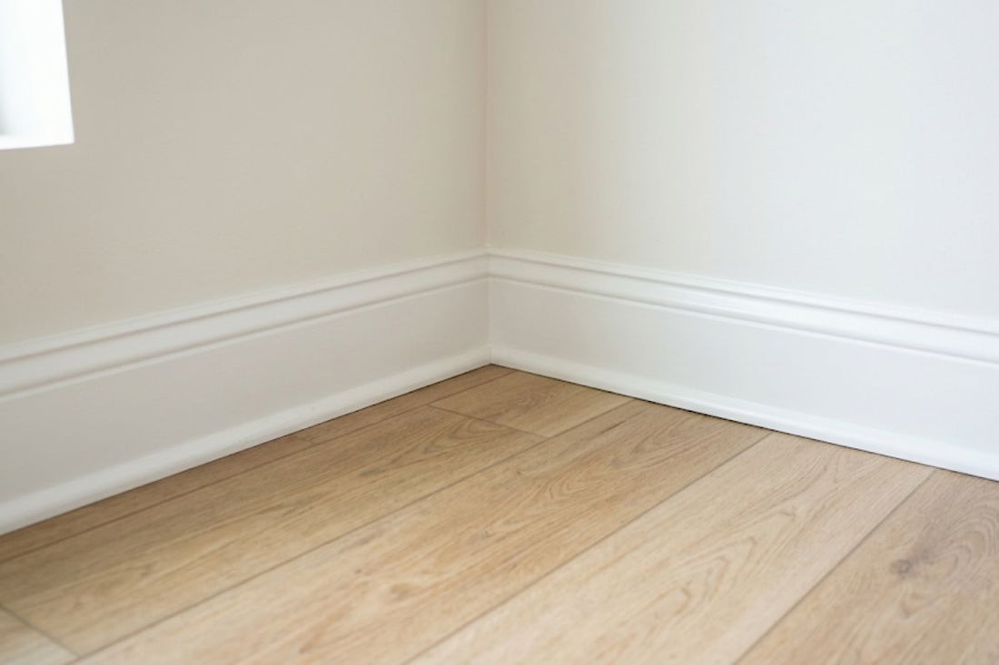 White painted baseboard meeting light oak toned vinyl plank flooring in a room corner
